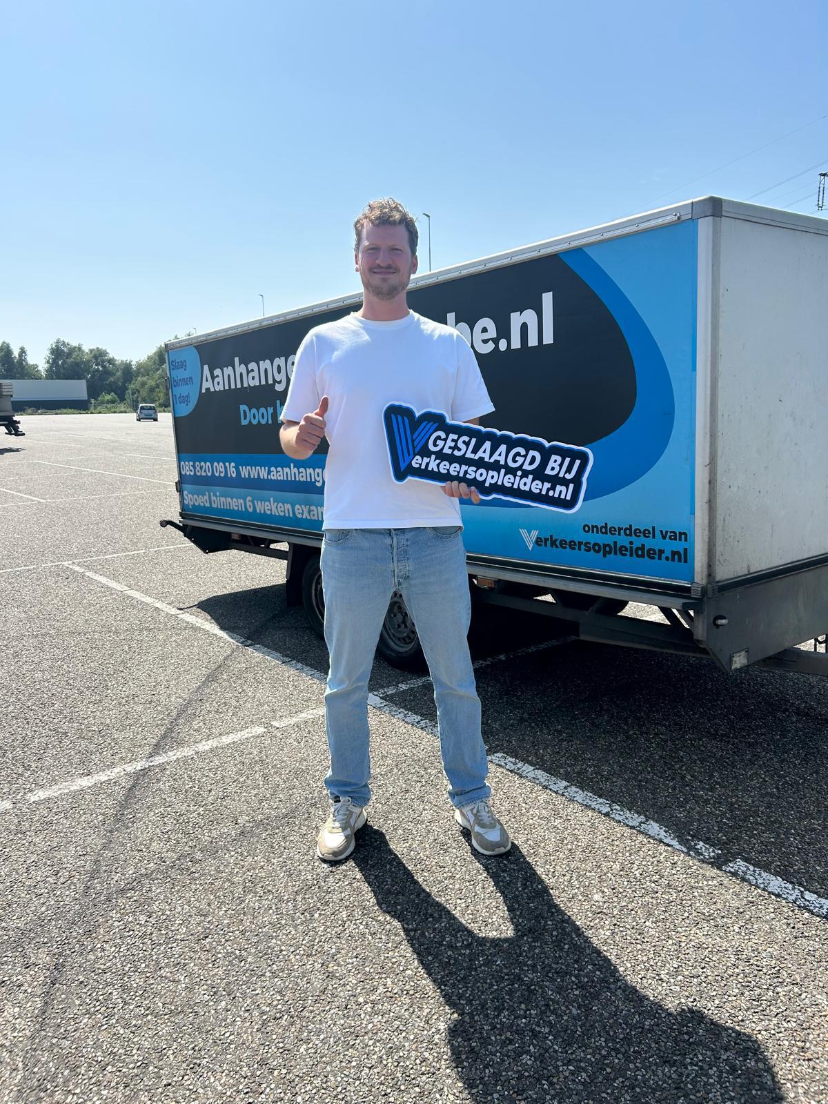 Geslaagde cursist staat met een geslaagd-bord voor een lesvoertuig met aanhanger tijdens de BE-rijbewijs cursus in Rotterdam.
