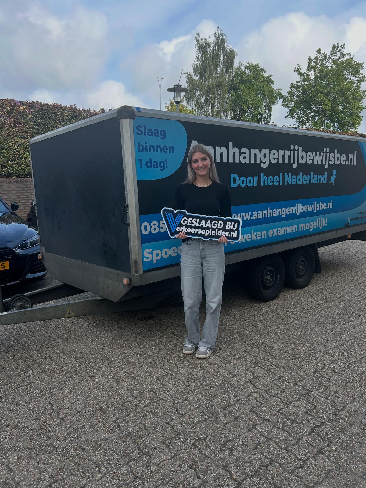 Cursist poseert met geslaagd-bord voor een aanhanger na de BE-rijbewijs opleiding in Rotterdam.