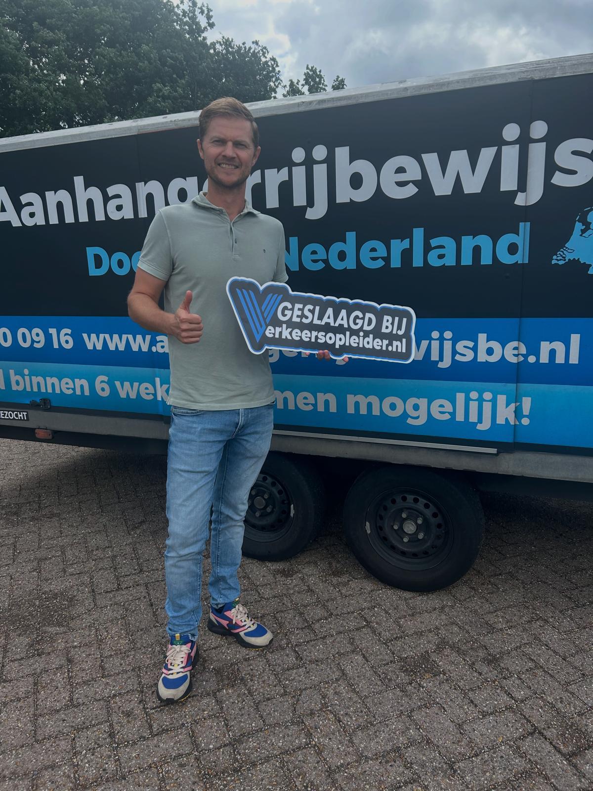 Geslaagde cursist staat voor het lesvoertuig met aanhanger na succesvolle BE-examentraining in Rotterdam.